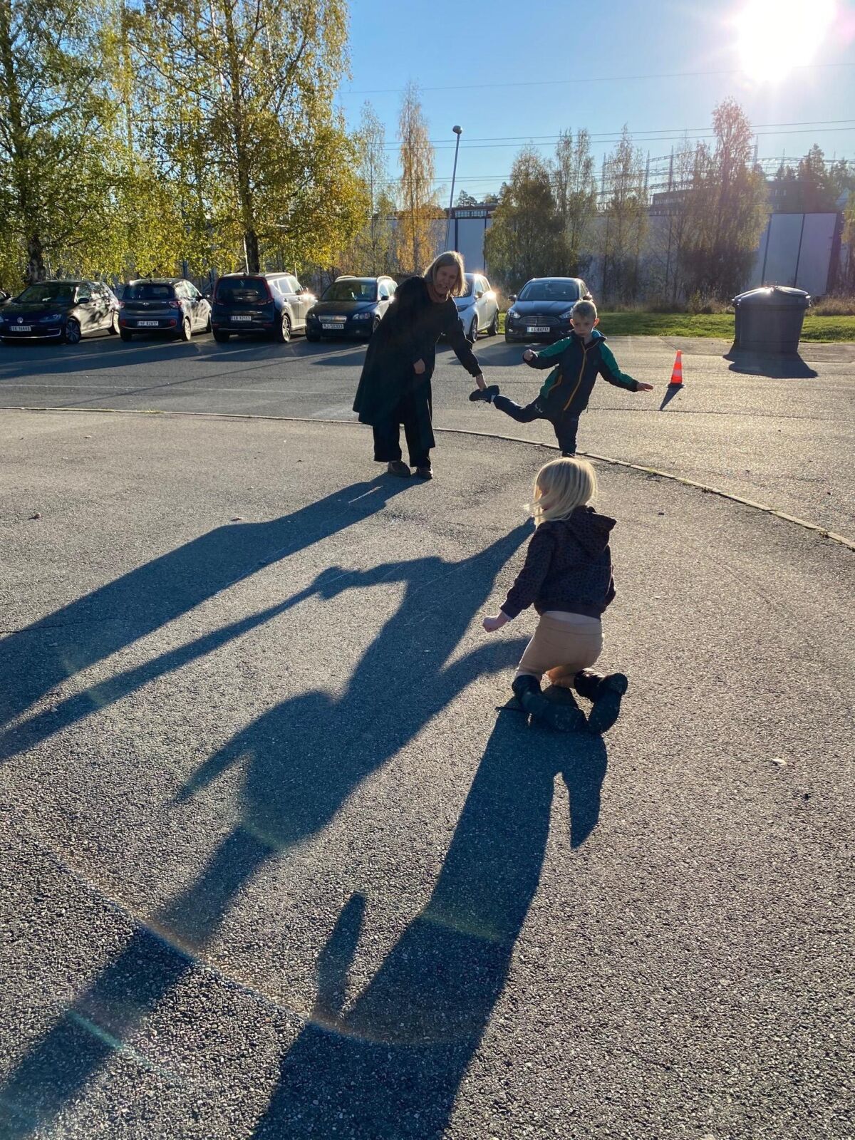 En av kunstnerne står i skolegården med to barn som leker med skyggen sin. Foto