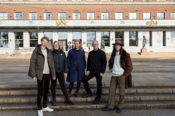 Portrett av fem utvalgsmedlemmer stående på trappen foran rådhuset ved sjøsiden. Foto