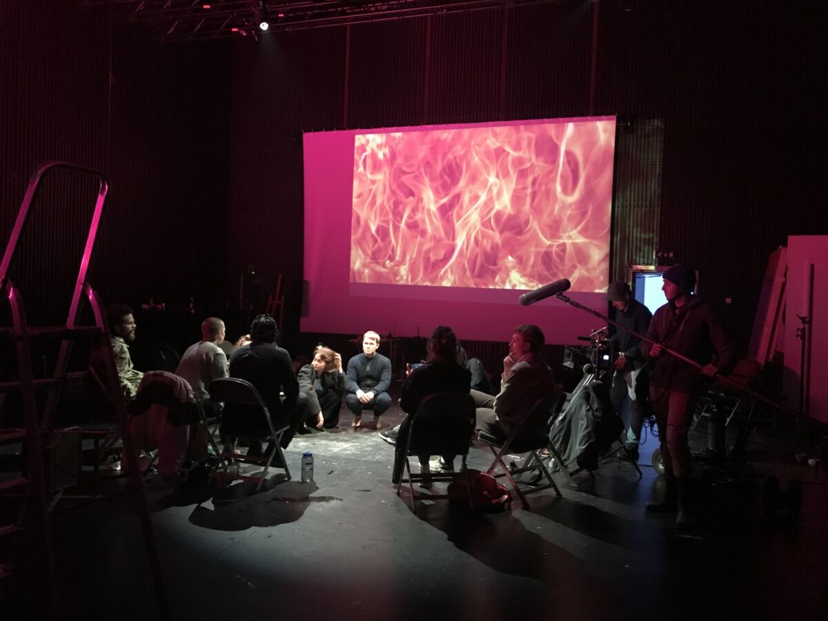 En gruppe sitter i en blackbox i ring, og ser på bilder på en prosjektor. Stillbilde fra film.