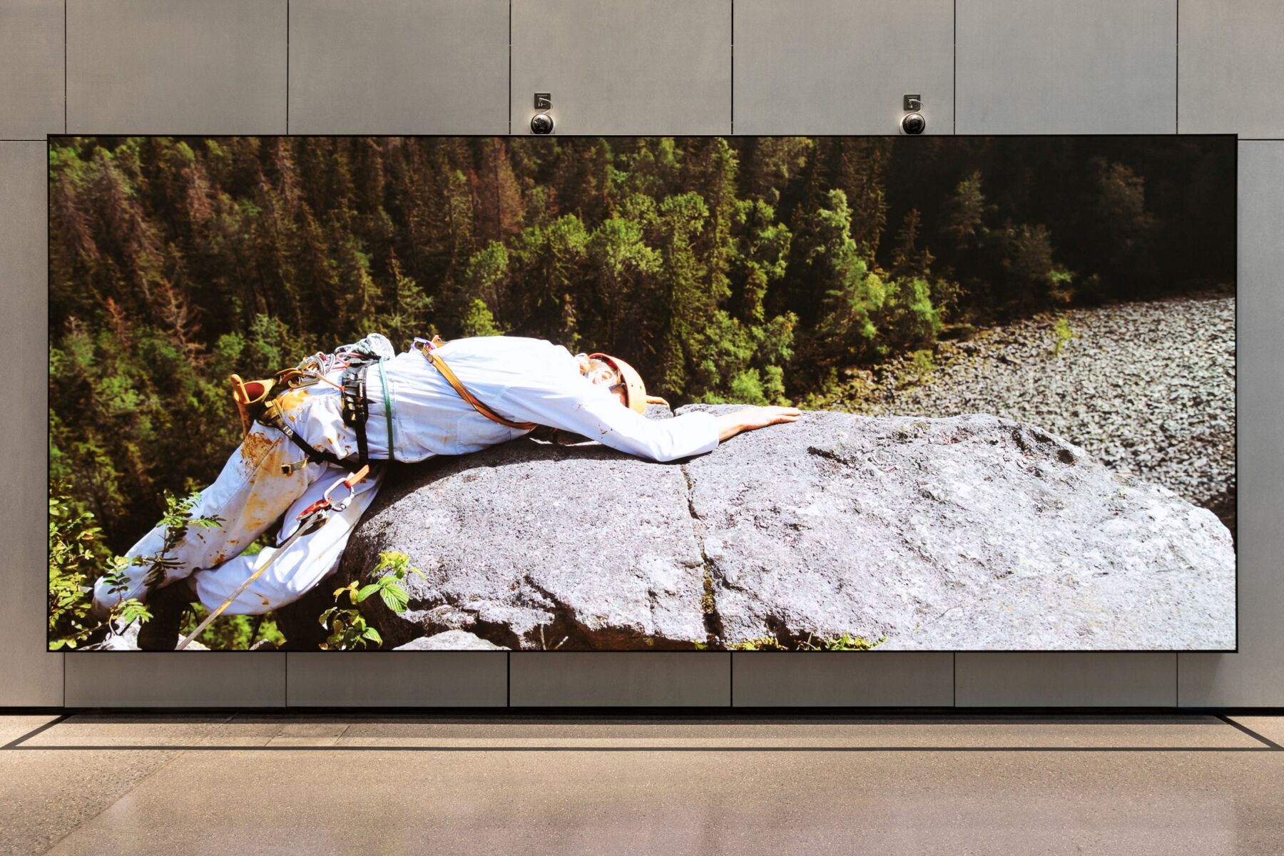 Et foto av et bilde hvor en person ligger på en stein ute i naturen. Foto.