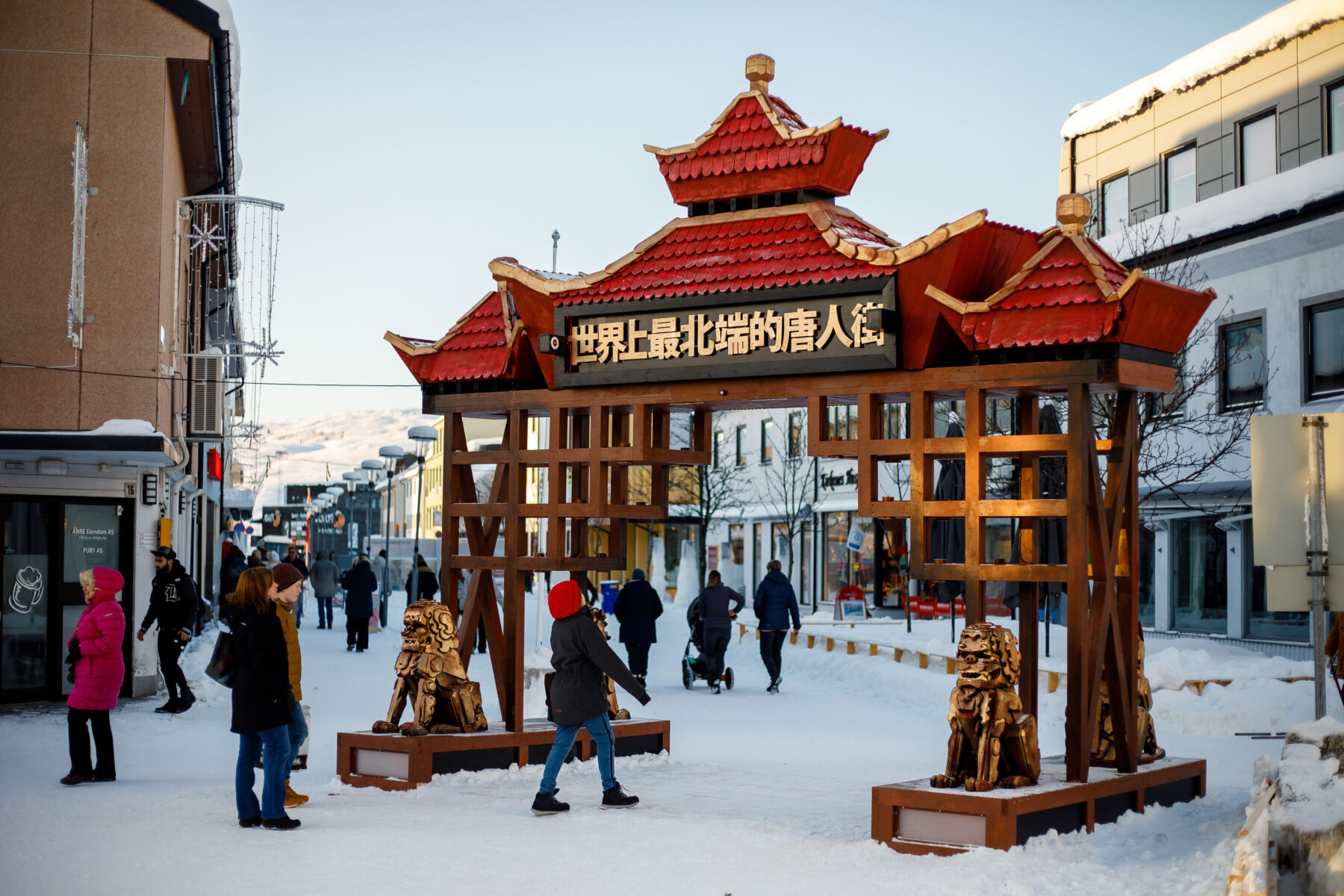 En portal med dekorasjon og kinesiske bokstaver stående i en snølagt handlegate. Foto.