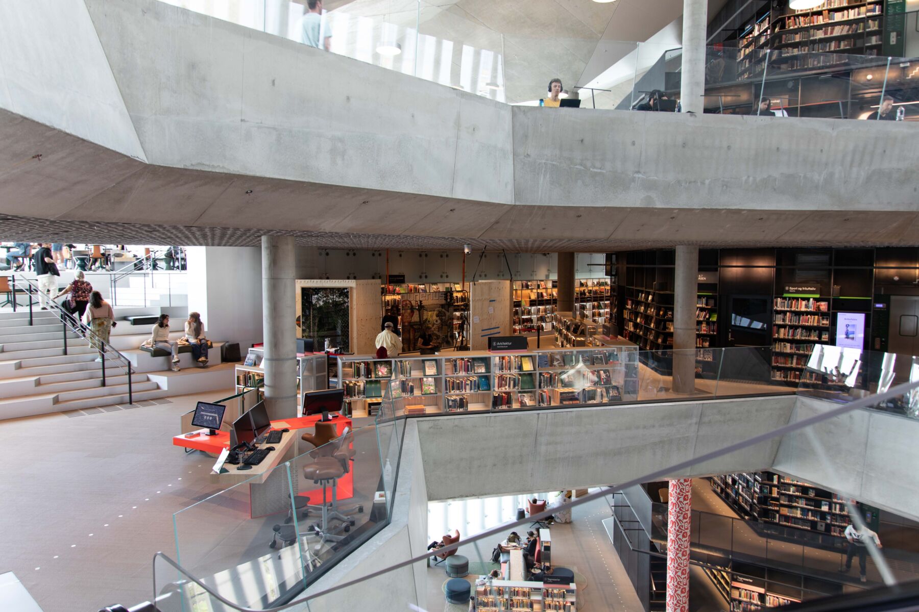 Oversiktsbilde av et bibliotek med mange personer som leser, går, sitter eller snakker. Foto.