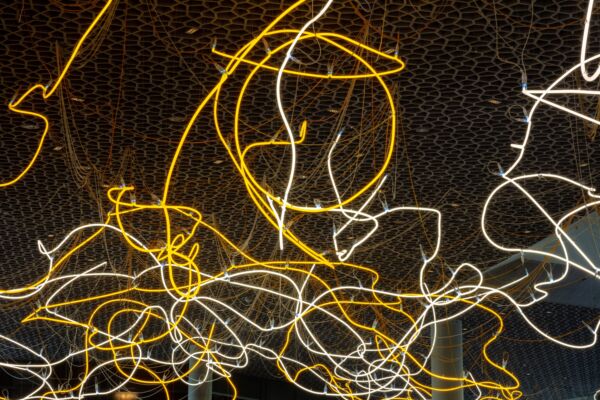 Lysinstallasjon hengende fra taket i et stort bibliotek. Foto.