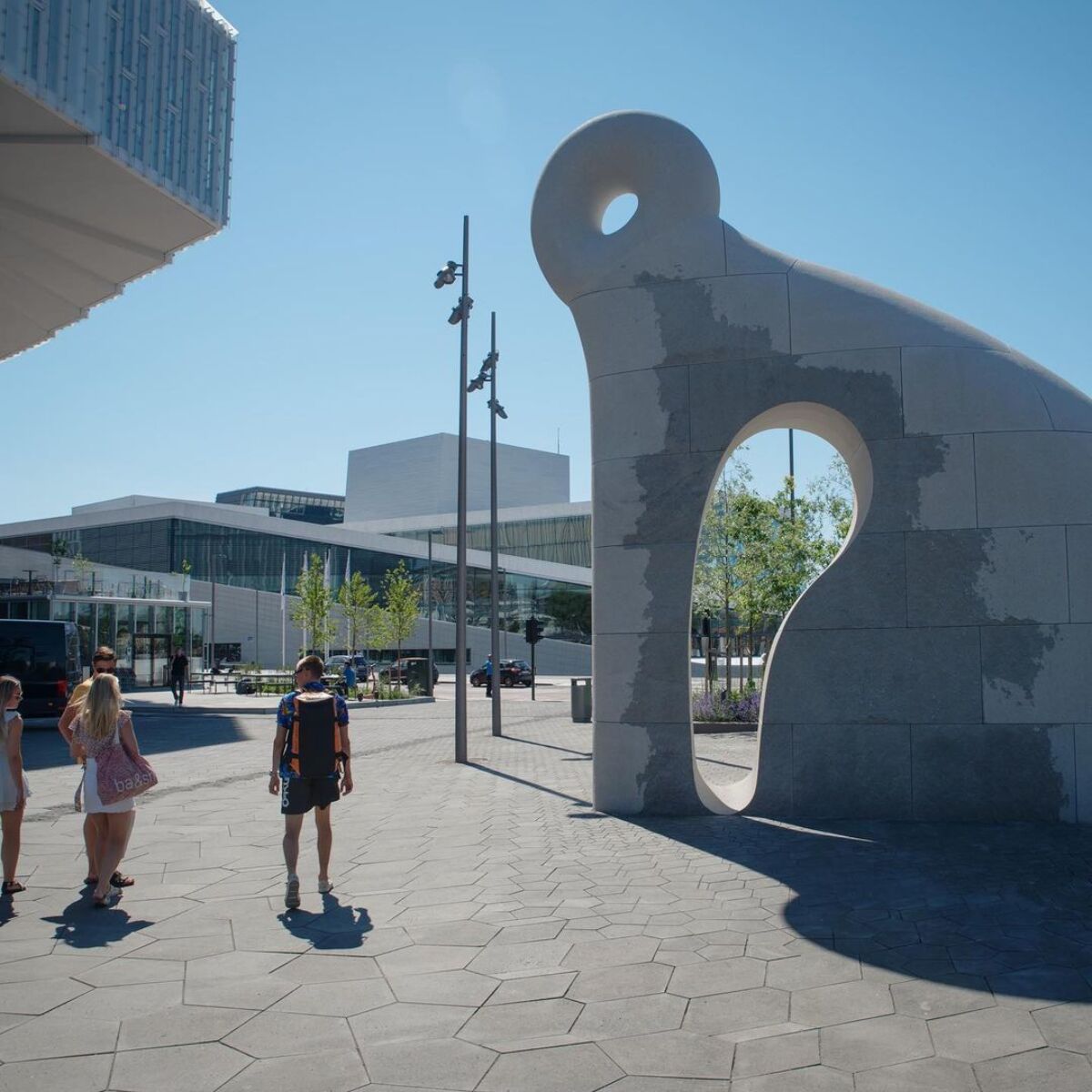 Tre publikummere ser på skulptur utenfor Deichman Bjørvika, med Operabygget i bakgrunnen.