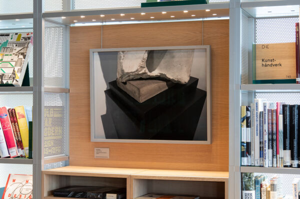 Foto av et foto i svart-hvitt hengende i en nisje i Deichman Bjørvika med bøker i hyllene rundt.