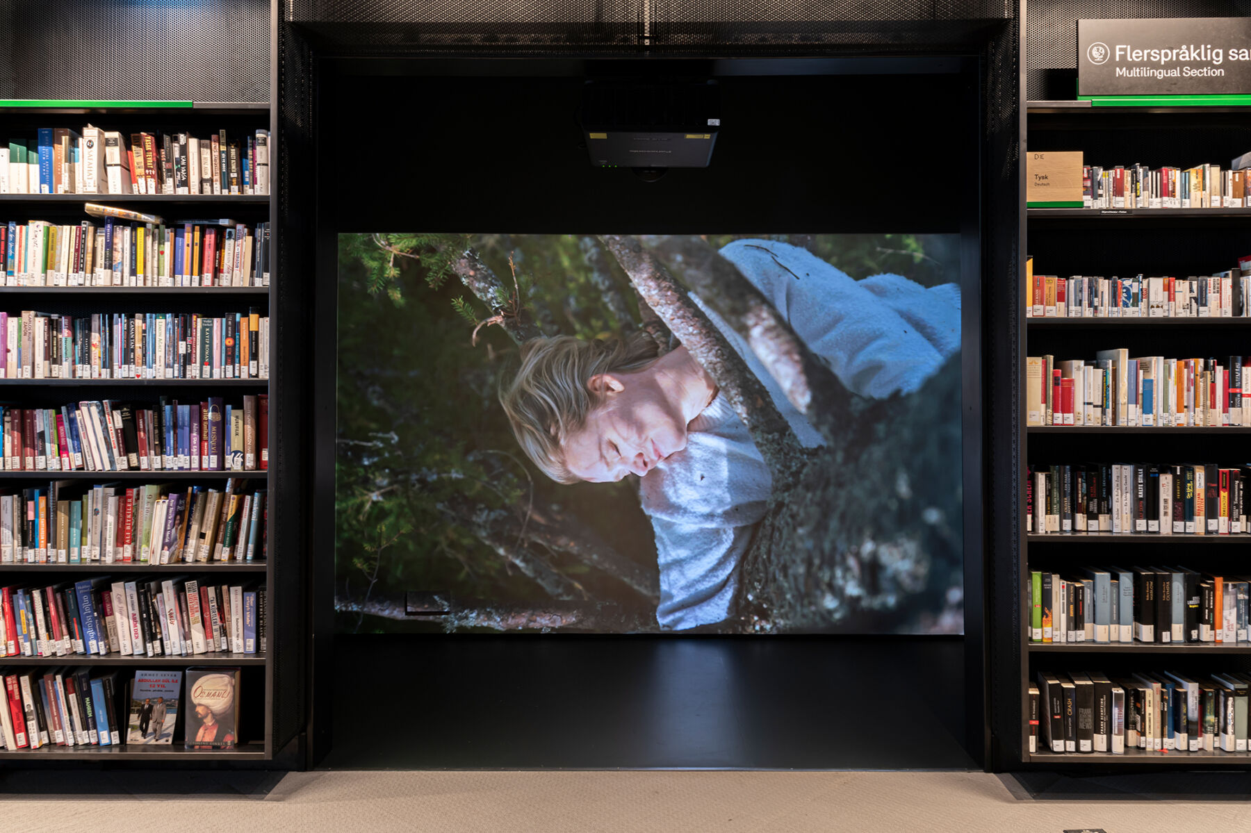 Bilde viser projisering av film på skjerm i biblioteket, i et avlukke flankert av bokhyller. Foto