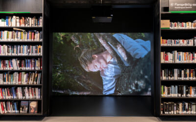 Bilde viser projisering av film på skjerm i biblioteket, i et avlukke flankert av bokhyller. Foto