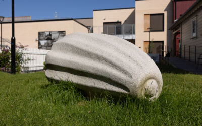 Skulptur av frø står på en gressplen. Foto.