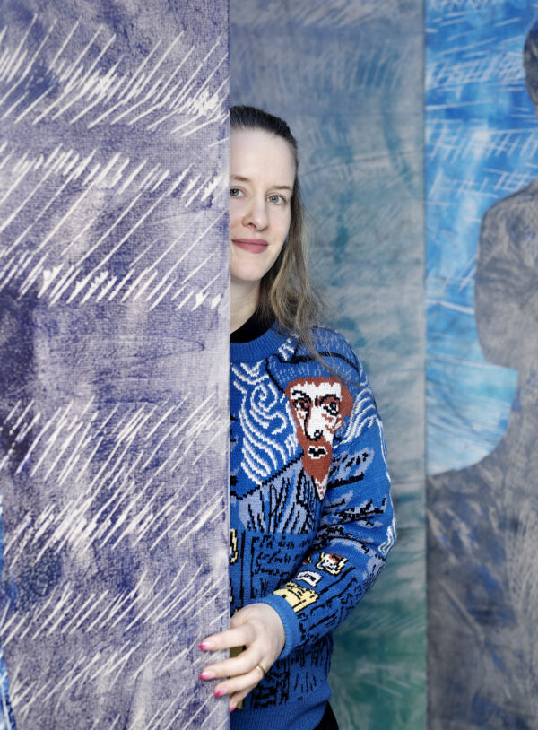 Portrettfoto av person som halvveis skjuler seg bak et kunstverk.