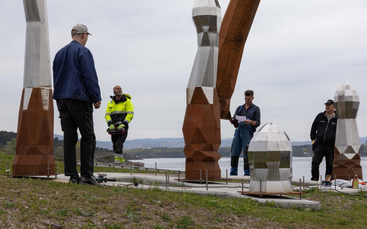 4 personer er i arbeid med å montere en skulpturgruppe på Langøyene. Foto