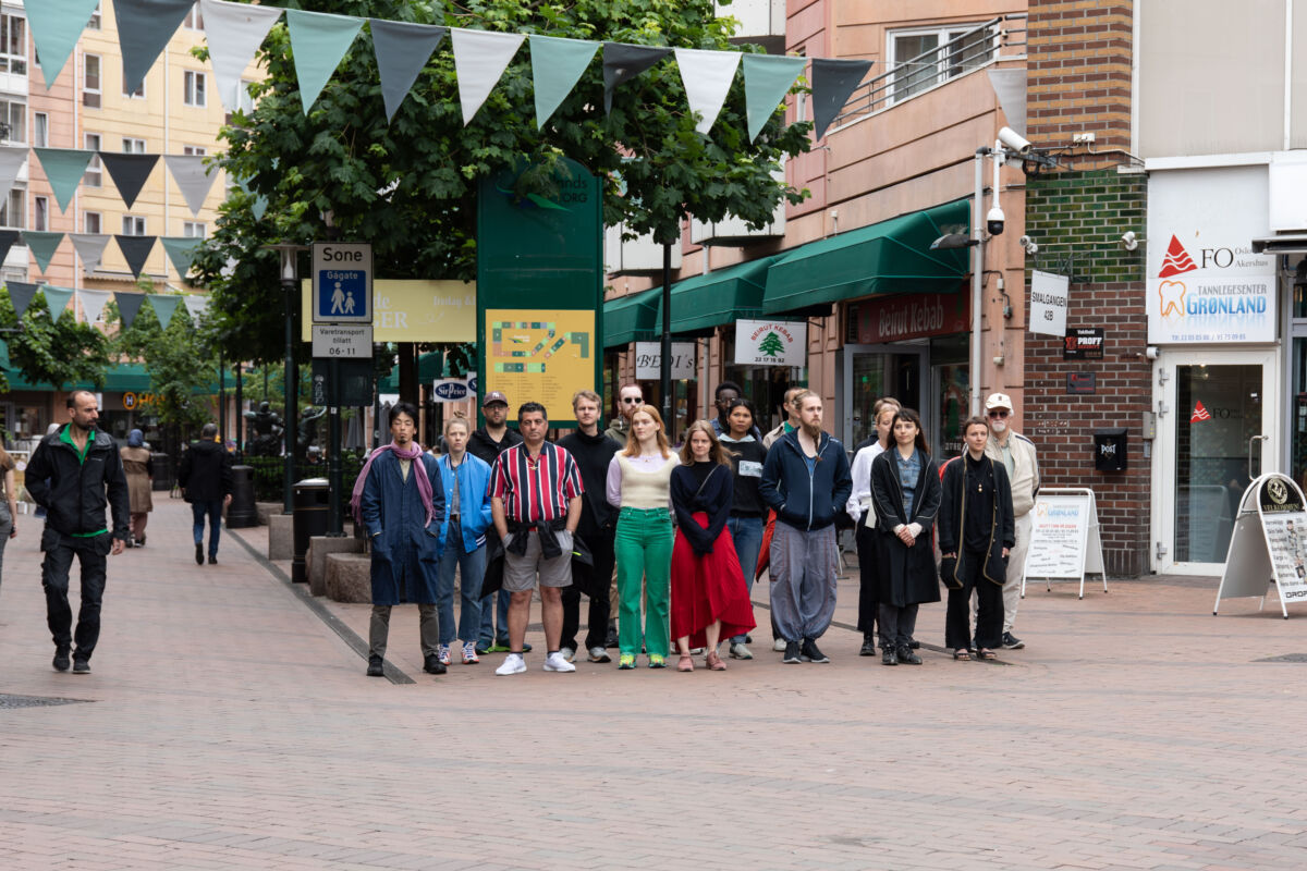 En gruppe mennesker står oppstilt på bytorg og titter ut i luften. Foto