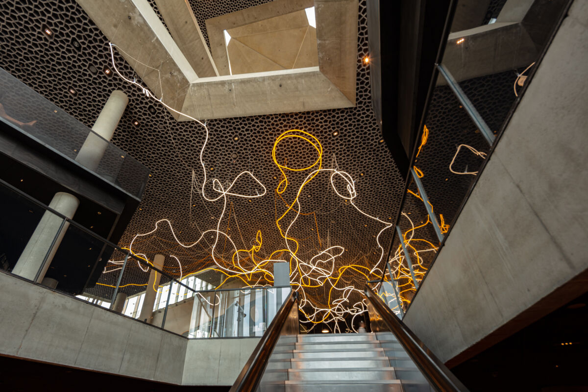 Stair, concrete and artwork in neonlight hanging from the celing. Photo.