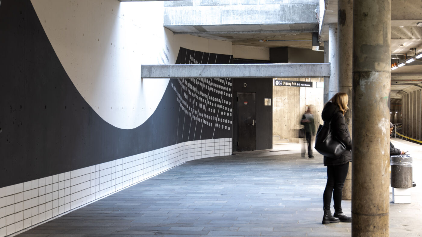 T- banestasjon, kunstverk oppmalt på vegg, mennesker venter å perrongen. Foto