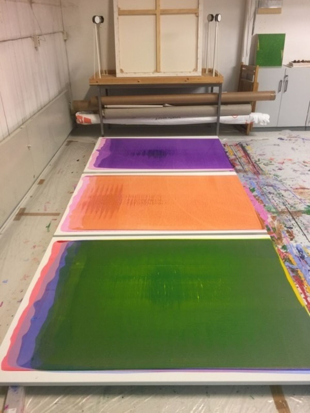 Tre fargerike malerier ligger på et gulv.