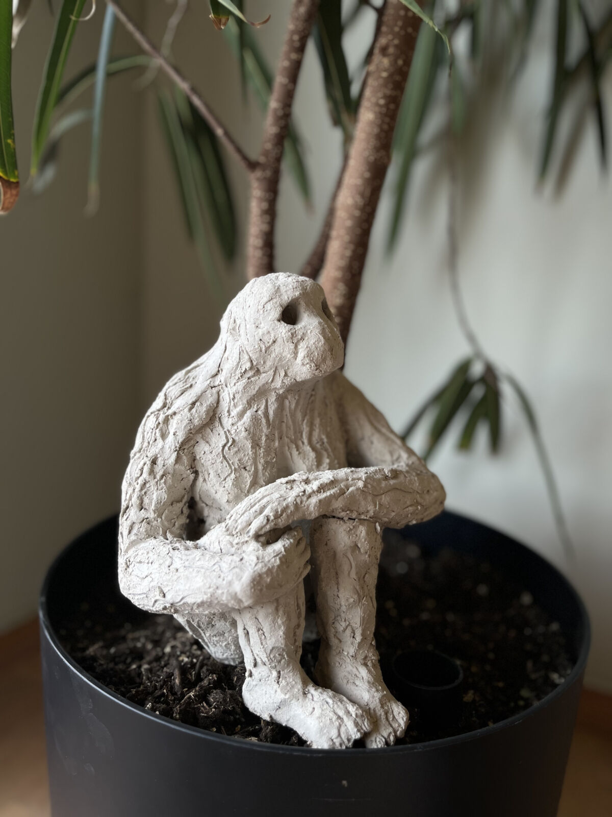 Modell av apelignende skulptur som sitter i en blomsterpotte. Foto.