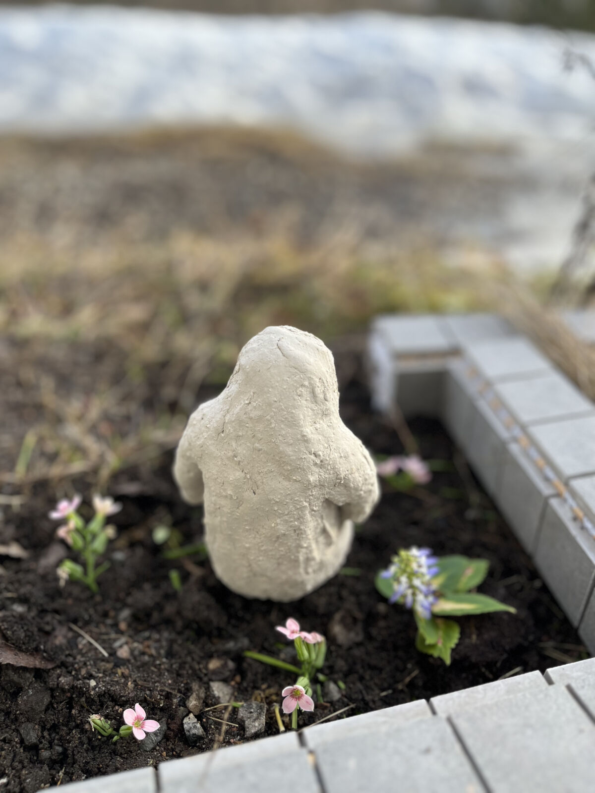 Modell av apelignende skulptur som sitter i et blomsterbed. Foto.