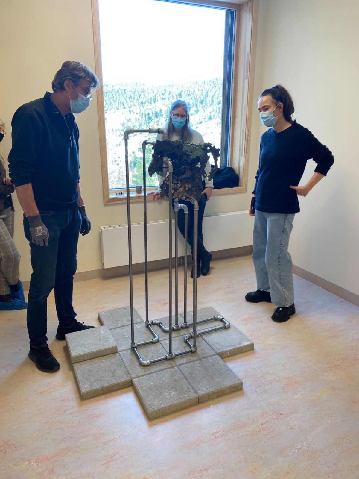3 mennesker står rundt skulptur i rom. Foto