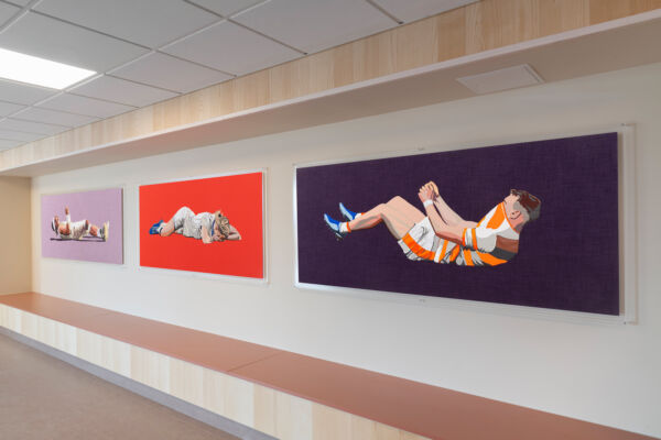 Tre malerier av tre mennesker i idrettstøy. Maleriene henger på veggen over en sittenisje. Foto.