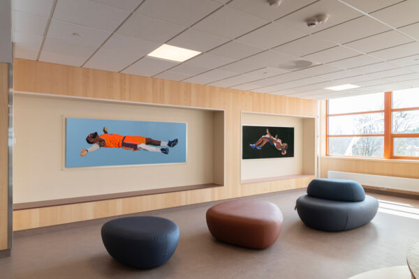 To malerier henger inni hver sin sittenisje i et oppholdsrom på en skole. Foto.