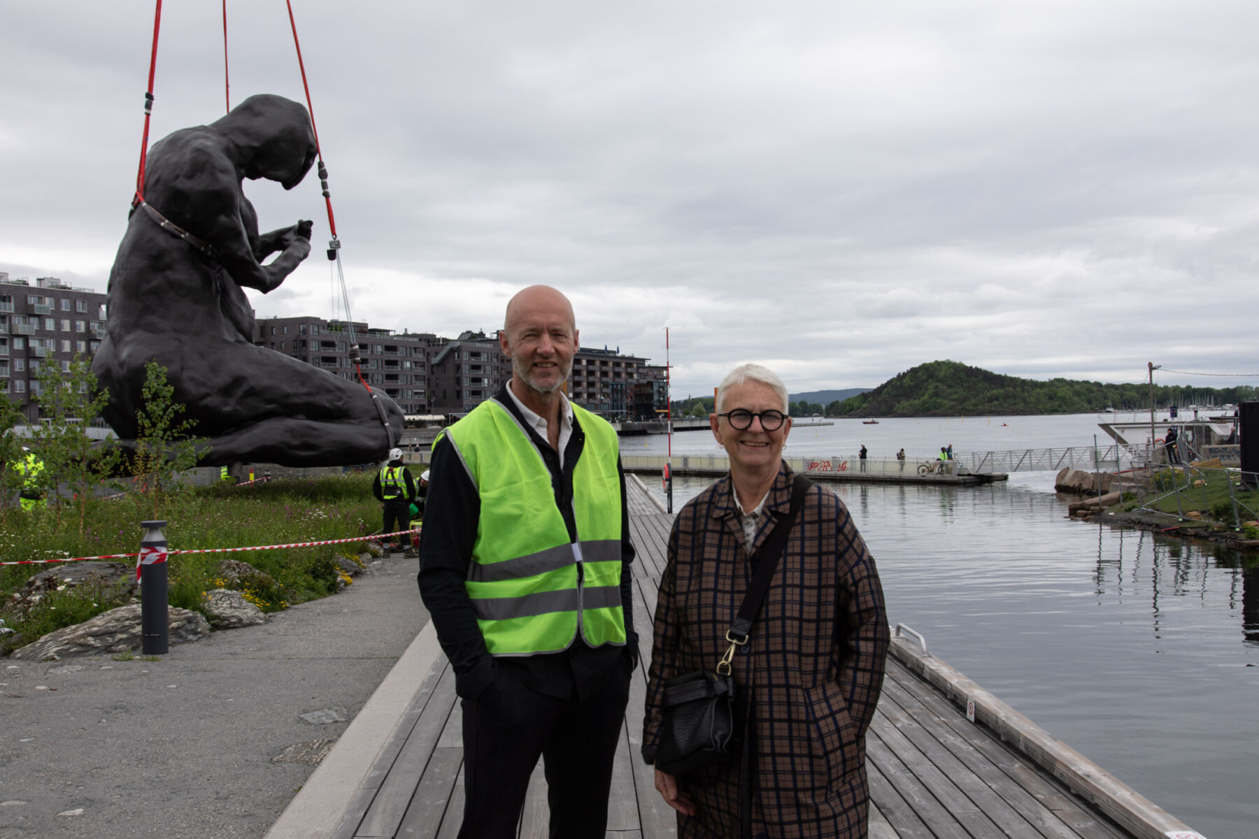 To personen se i kamera, i bakgrunnen senkes en stor bronseskulptur ned i en eng. Foto