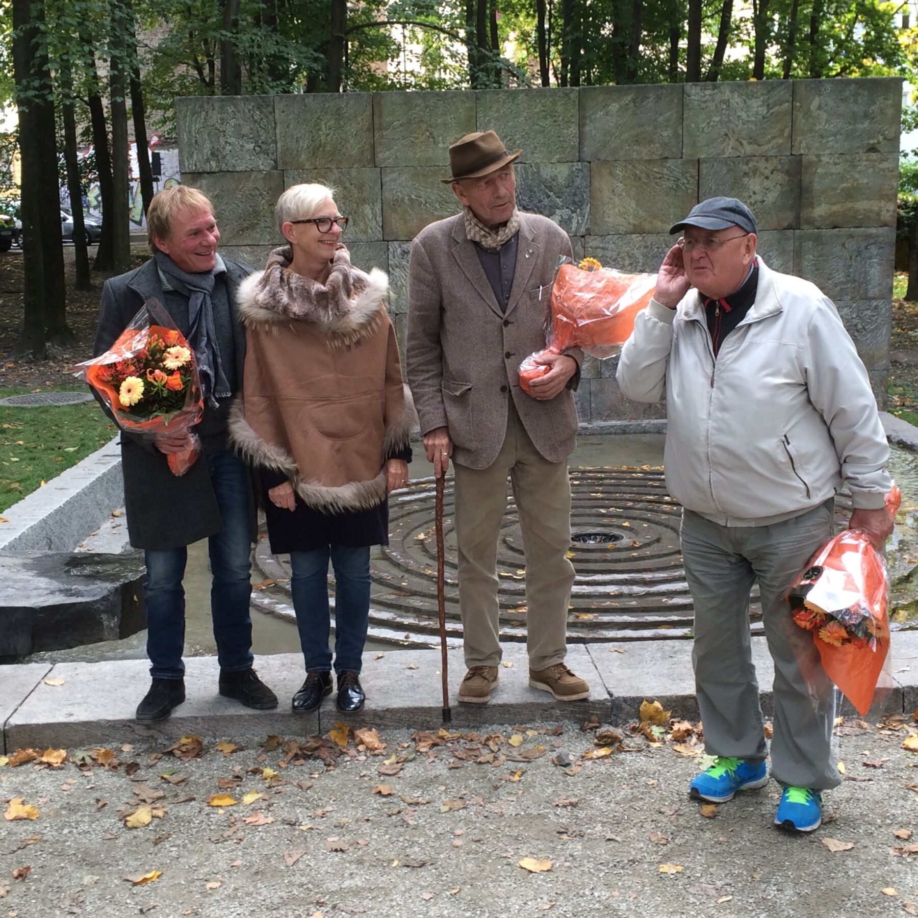 Fire personer står foran en spiralformet fontene i Klosterenga park. Tre av dem holder en blomsterbukett. Foto