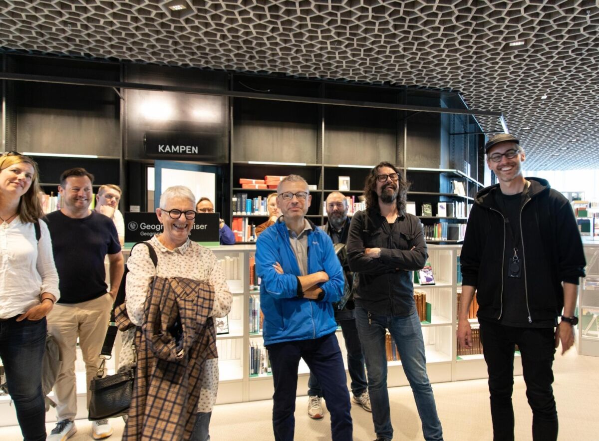 En gruppe smilende mennesker er på omvisning i utstilling på Deichman Bjørvika. Foto