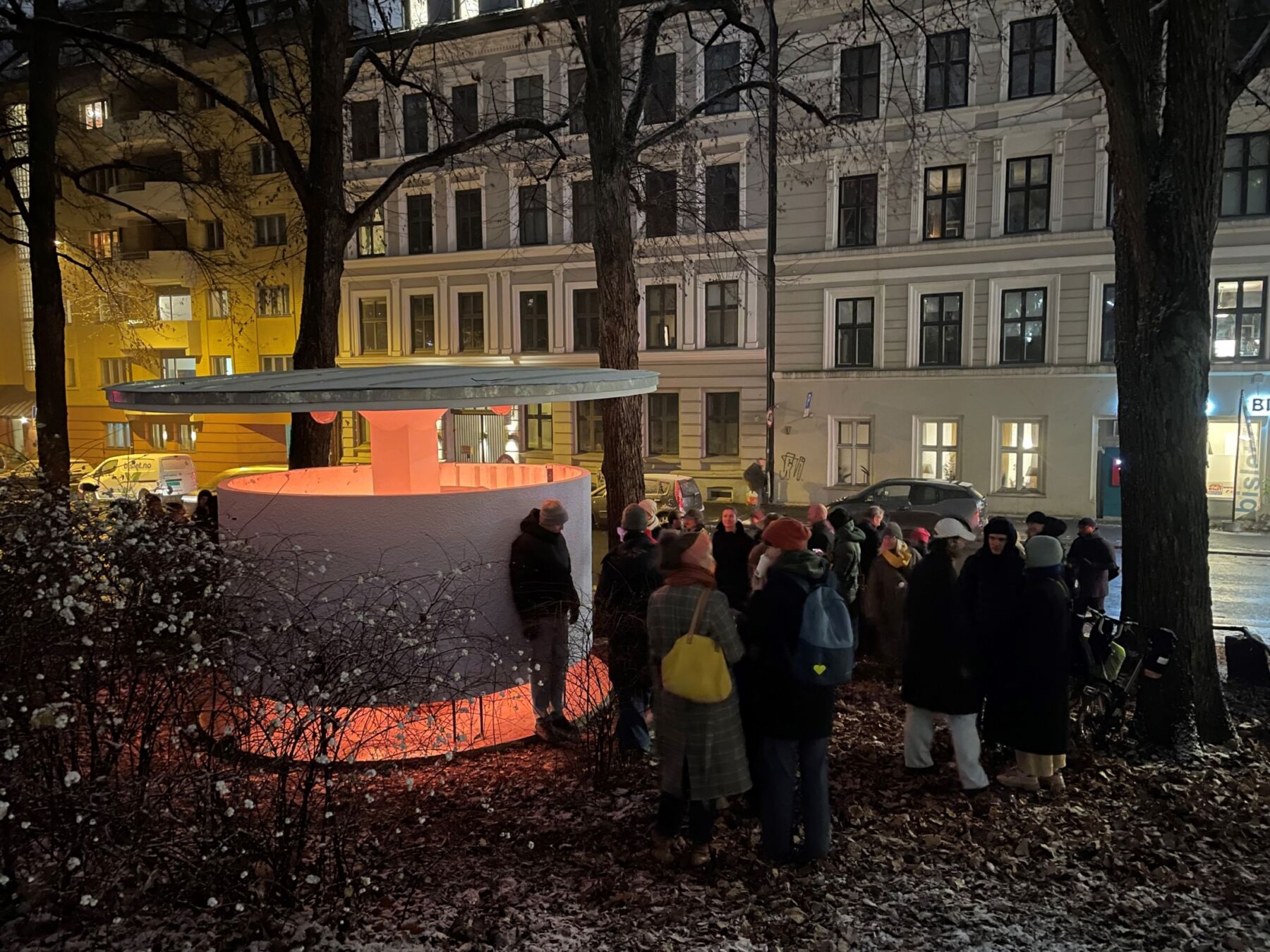 En stor gruppe mennesker står ved verket Kjærlighetskarusellen, vinterkveld. Foto