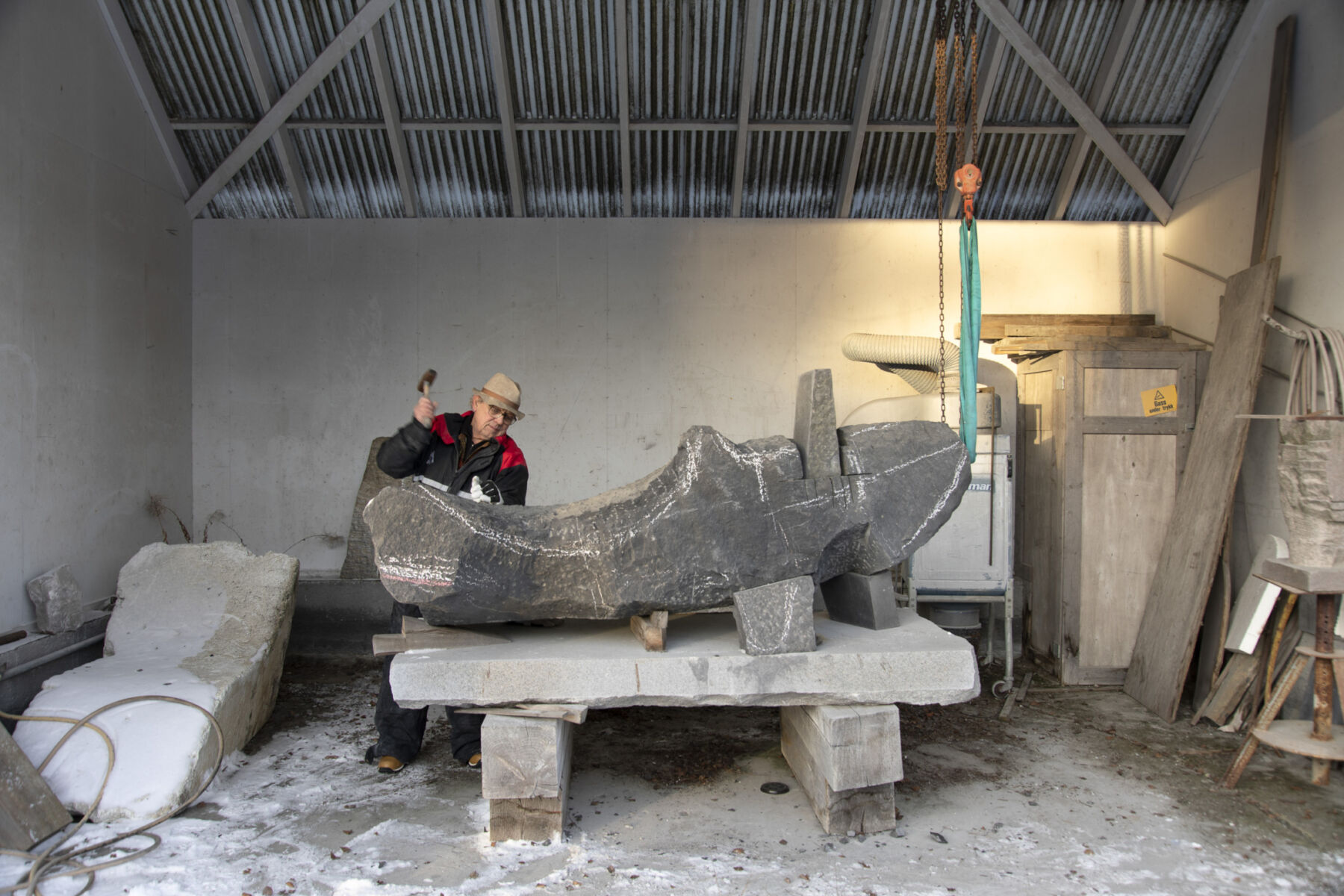 Kunstner Kristian Blystad hugger i stein i sitt uteatelier. Foto