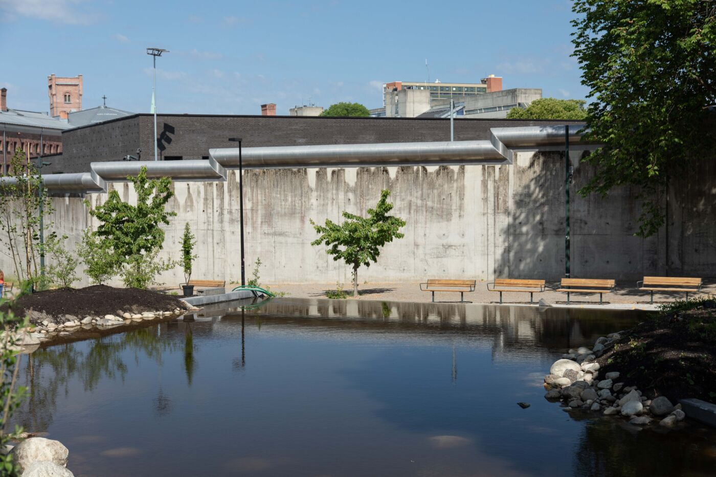 Vannspeil i forgrunn, benker, trær og fengselsmur i bakgrunn. Foto