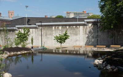 Vannspeil i forgrunn, benker, trær og fengselsmur i bakgrunn. Foto