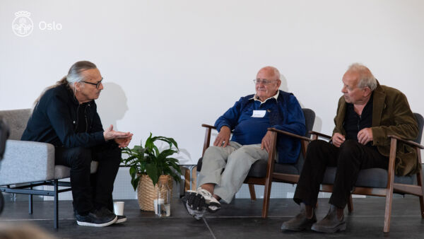 Foto av tre personer sittende på en scene. De har en samtale om kunst til Klosterenga park.