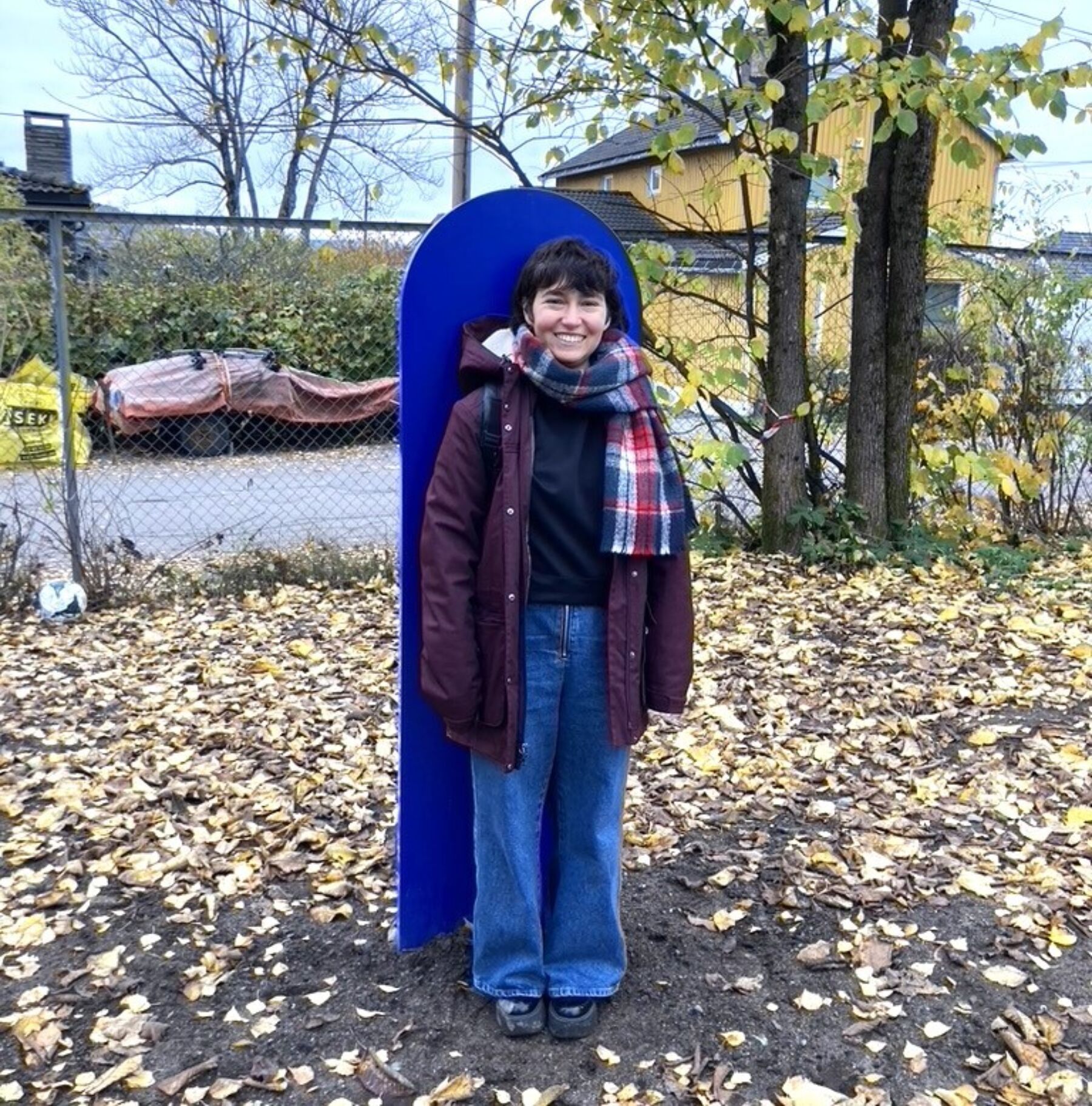 Foto av person som står foran en blå skulptur. Personen smiler mot kameraet.