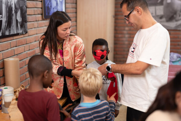 To voksne og tre barn står samlet rundt tekstil. Foto.