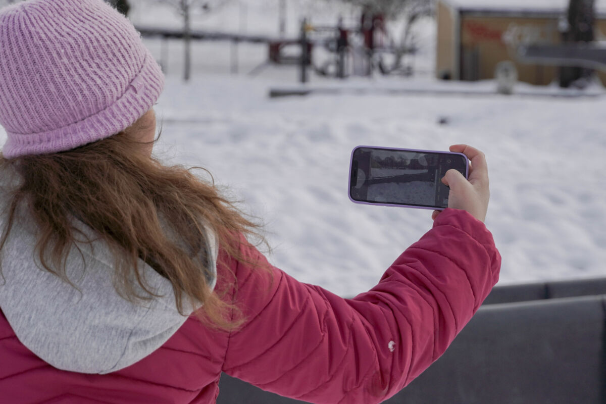 Barn står i en park og fotografer med mobiltelefonen. Foto.