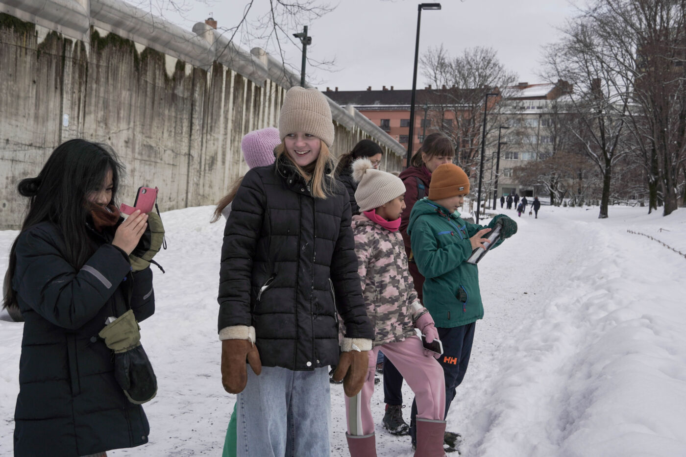 Flere barn står i en park og ser utover parken i snølandskap. Foto.