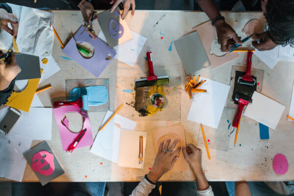 Barnehender rundt et bord som jobber med papir, tegnesaker, maling og mer. Foto.