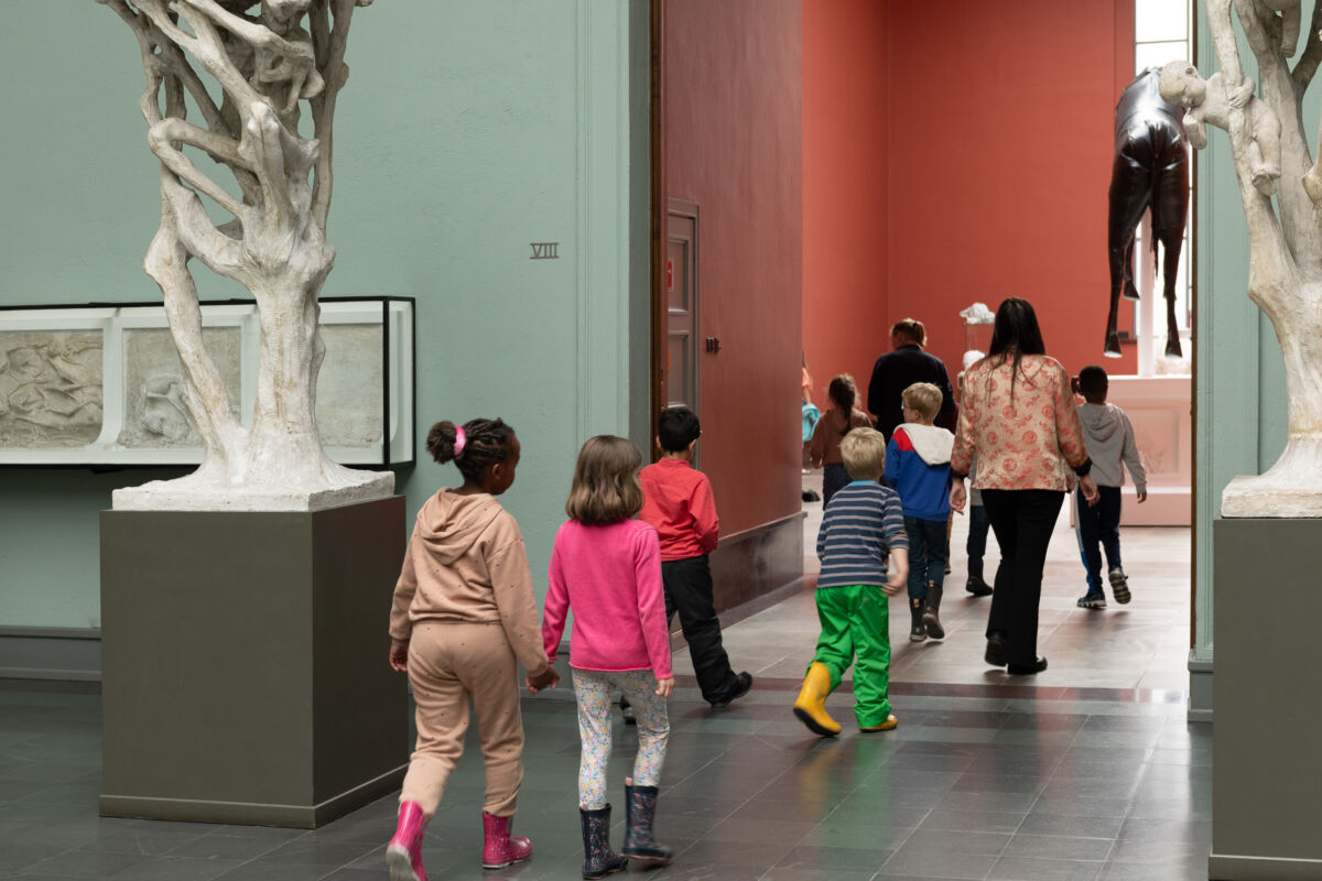 En gjeng med barn og to voksne går inne i et museum. De ser på kunst. Foto.