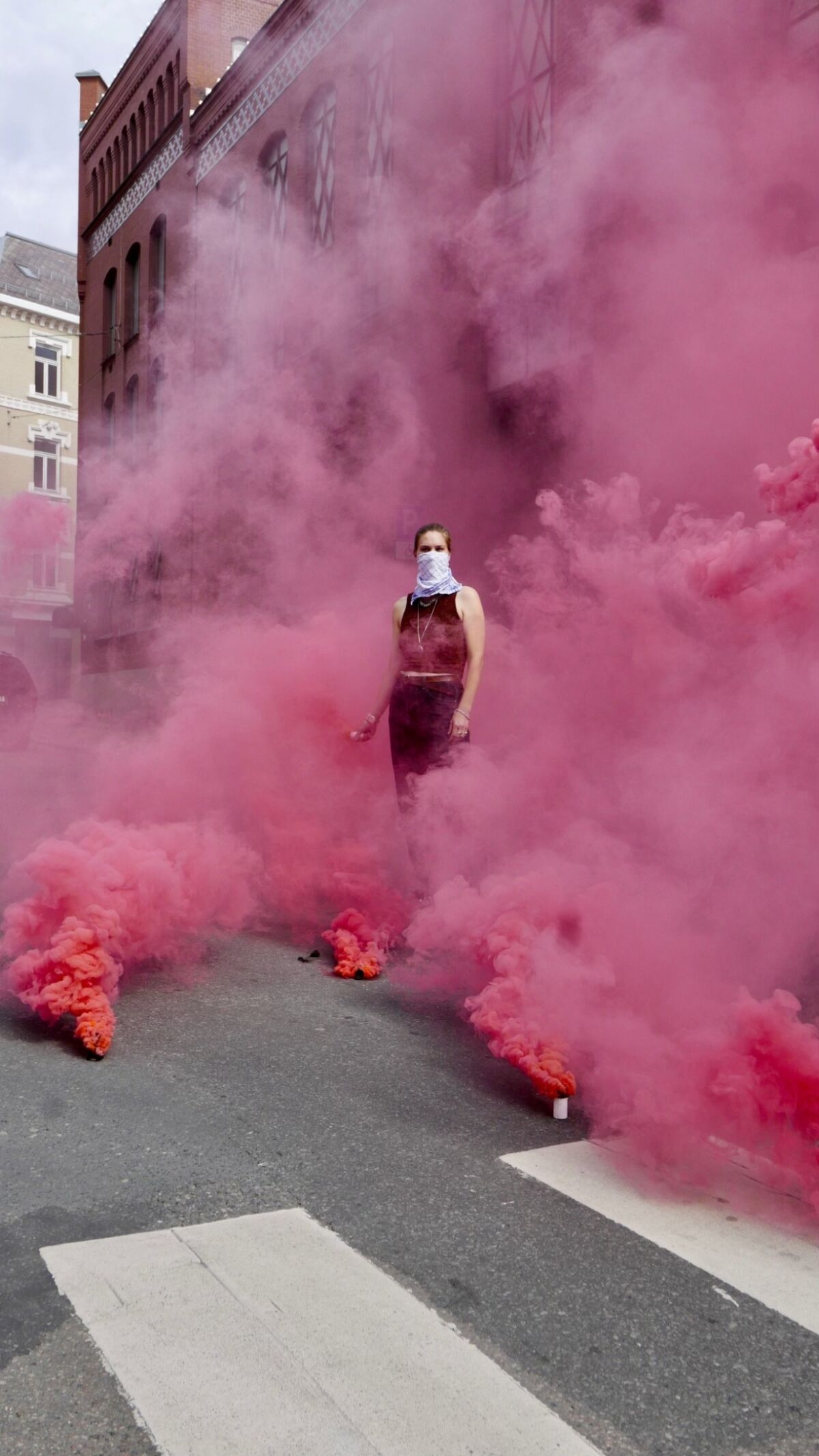 En person står i midten av bildet, omgitt av rosa røyk. Foto.