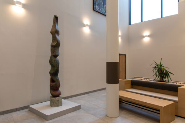 Foto av en lang og smal skulptur med organiske former. Stående i et stort, åpent rom på Lambertseterhjemmet.