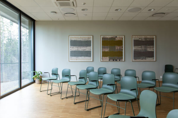 Foto av tre malerier hengt på en vegg i et rom fylt med stolrader.