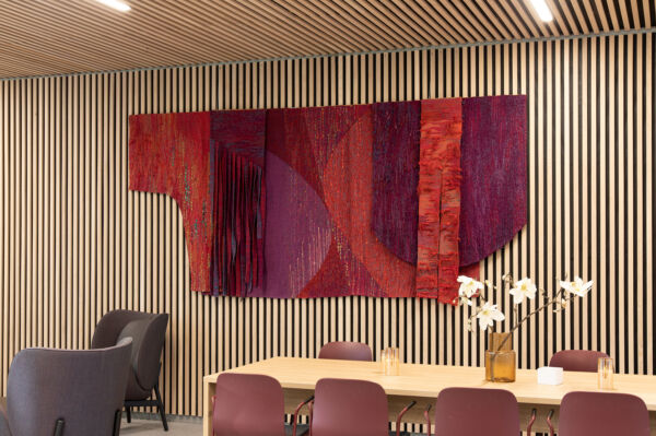 Foto av stort rødt tekstilverk hengende i et foajeområde på Lambertseterhjemmet.