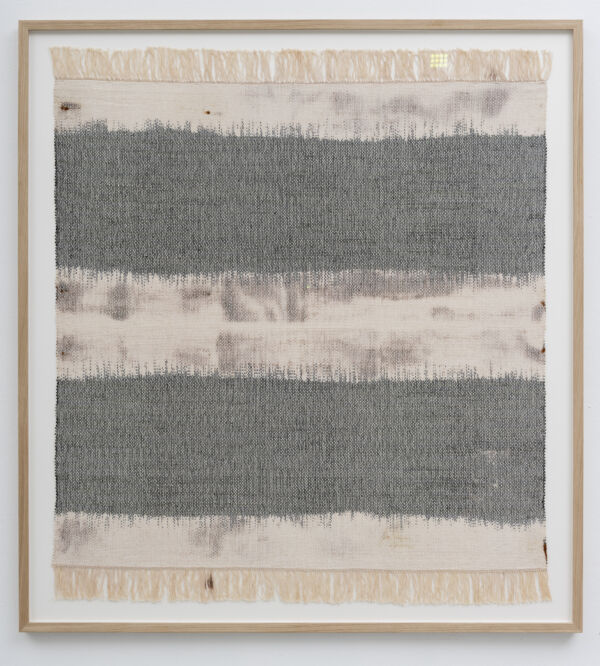 Foto av et kvadratisk tekstilverk, innrammet og hengende på en vegg.