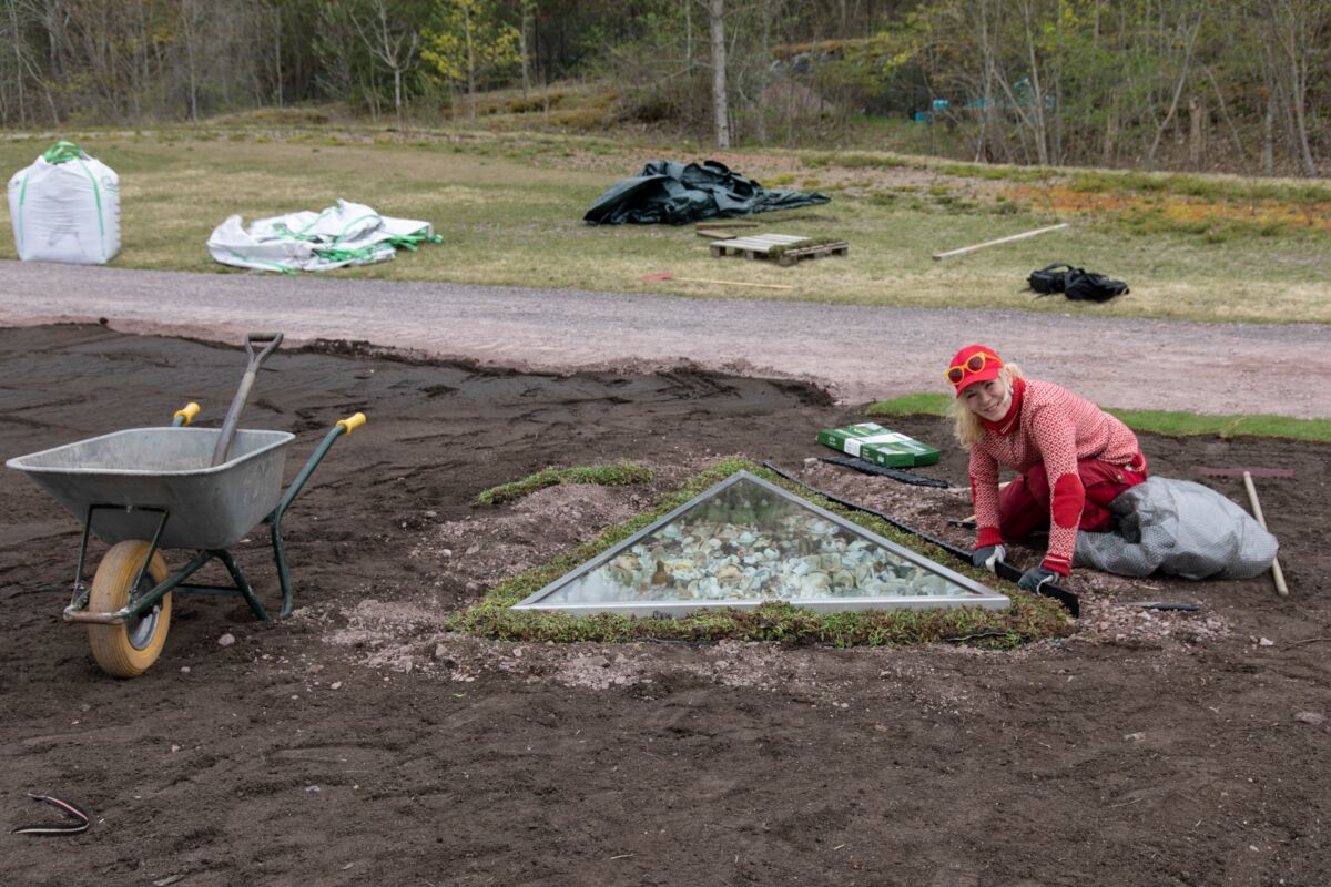 Person sitter på bakken og jobber i jorda. Foto.