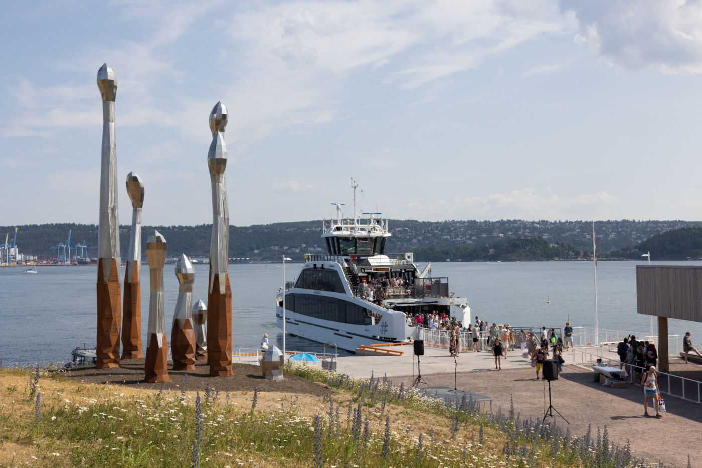 Kunstverk stående på en brygge. En båt i bakgrunnen. Foto.