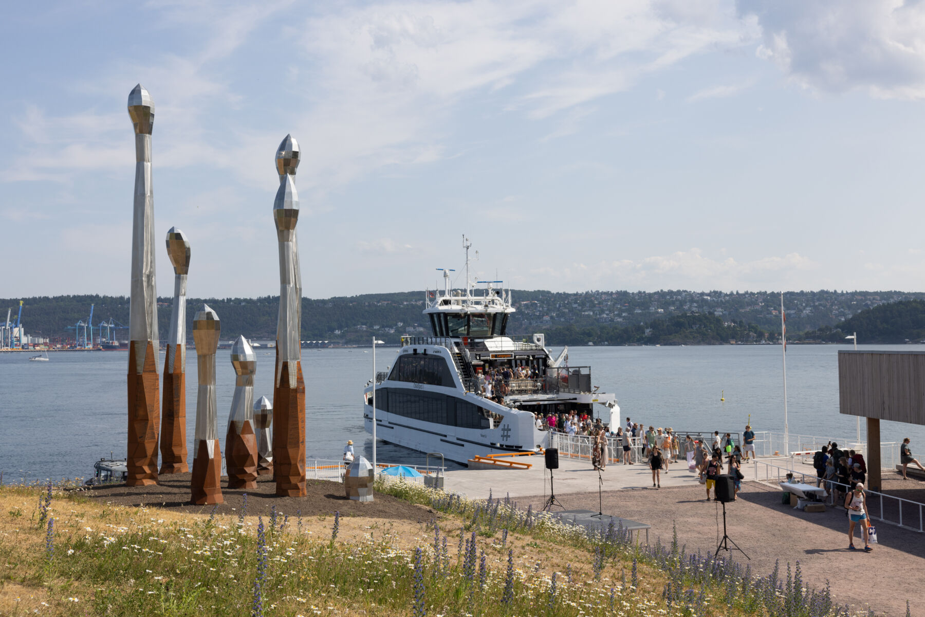 Kunstverk stående på en brygge. En båt i bakgrunnen. Foto.