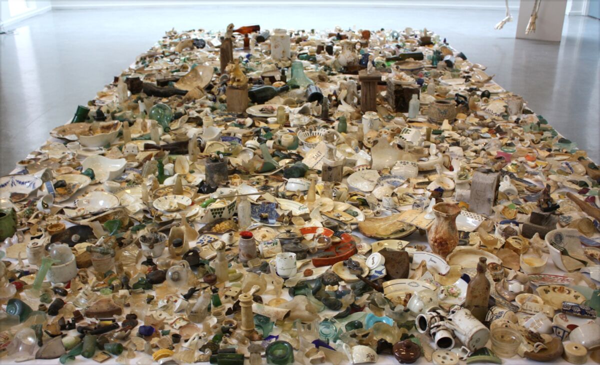 Kunstverk bestående av skatter fra strandsonen dekker gulvflate i et gallerirom. Foto