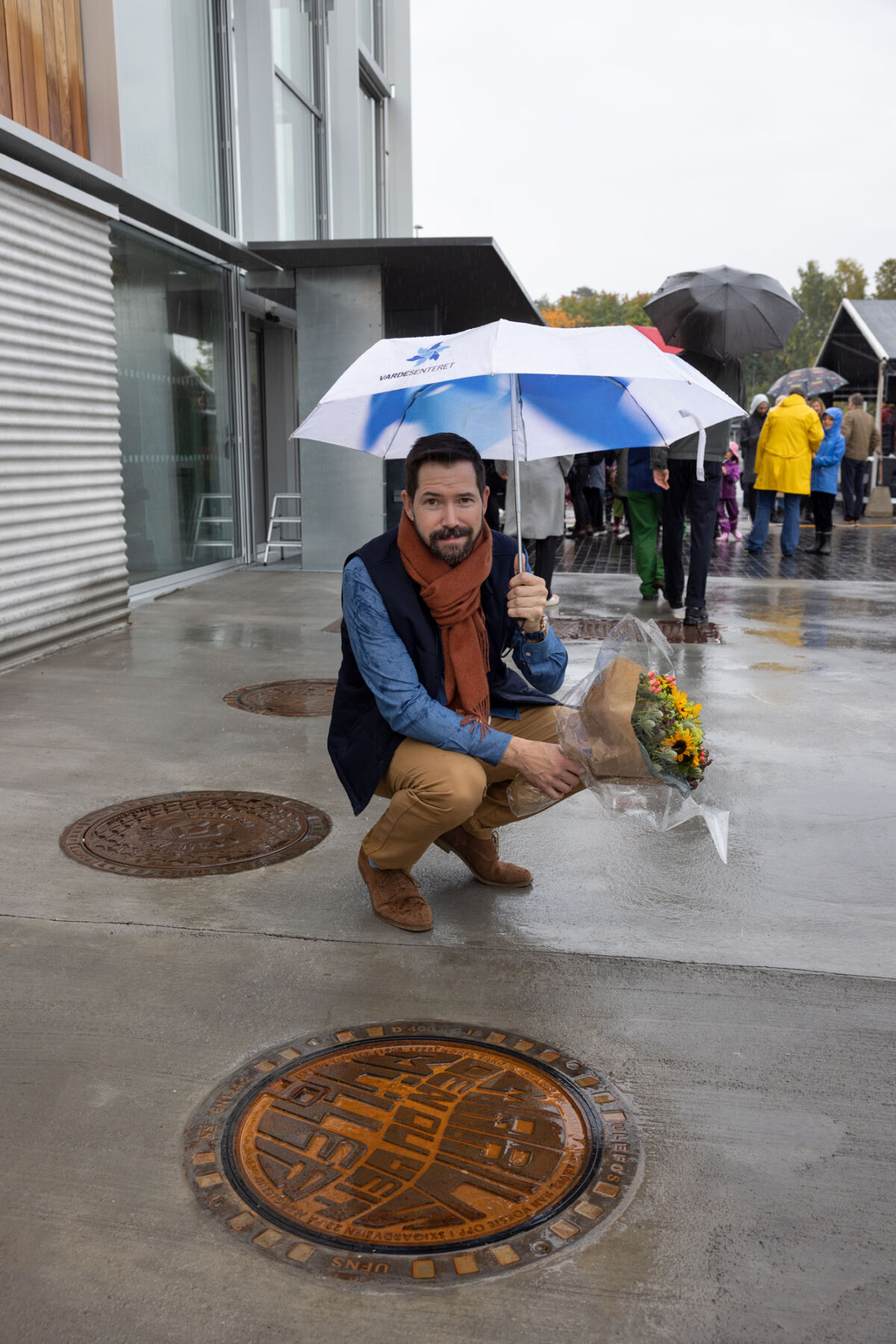 Kunstner Bjørn-Kowalski Hansen med en bukett solsikker ved kunstverk utført på kommelokk. Foto