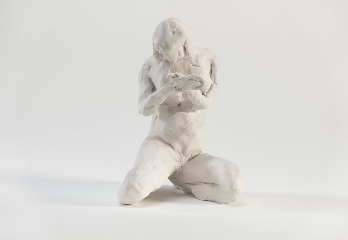 Figur av leire, kvinne som sitter på knærne og ser ned på hendene sine. Foto