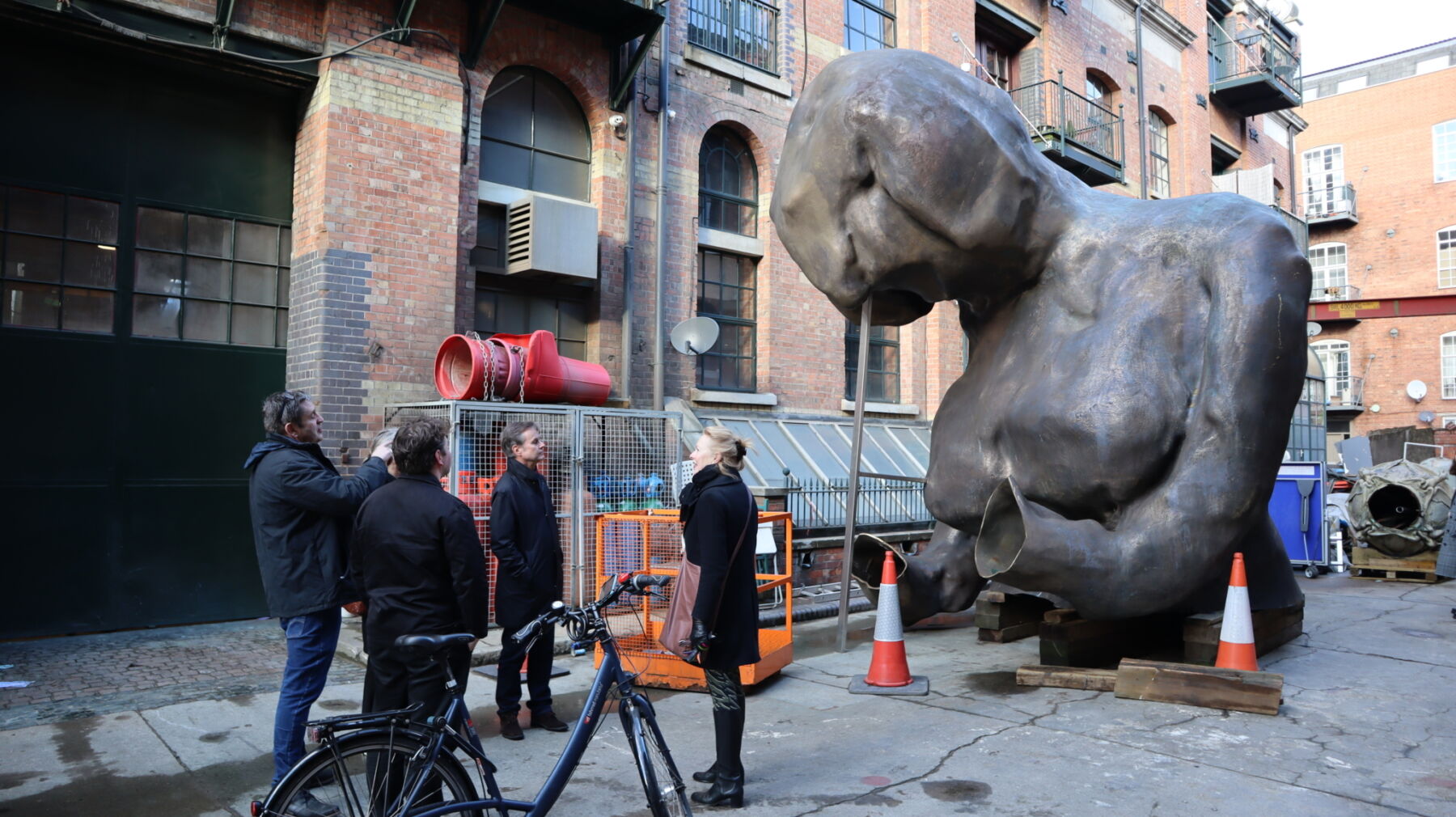 Del av skulptur, torso står ute på bakken, en gruppe mennesker står i forgrunnen. Foto