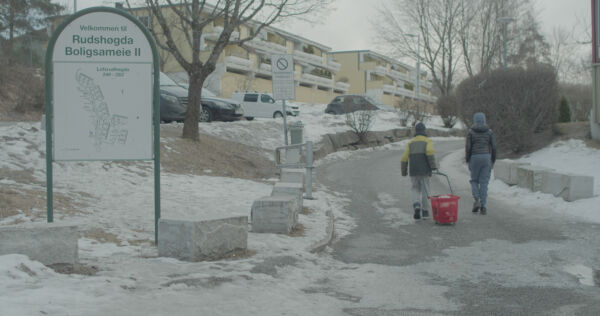 To personer går opp en vei mellom boligblokker i vinterlandskap. Foto.